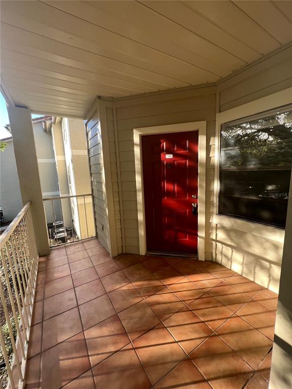 A covered balcony features tiled flooring, a red front door, and a metal railing — 3016 PARKWAY BOULEVARD UNIT 209, KISSIMMEE, FL
