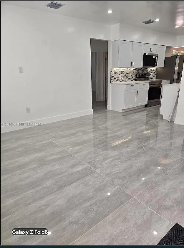 A kitchen with white cabinets and gray tiled floors opens into a living area — 13240 NE 4 Ave # 1, North Miami FL 33161, NORTH MIAMI, FL