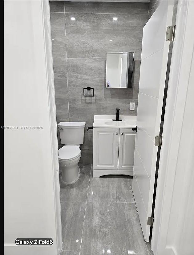 A small bathroom features gray tiled walls and floors, a white vanity, and a toilet — 13240 NE 4 Ave # 1, North Miami FL 33161, NORTH MIAMI, FL