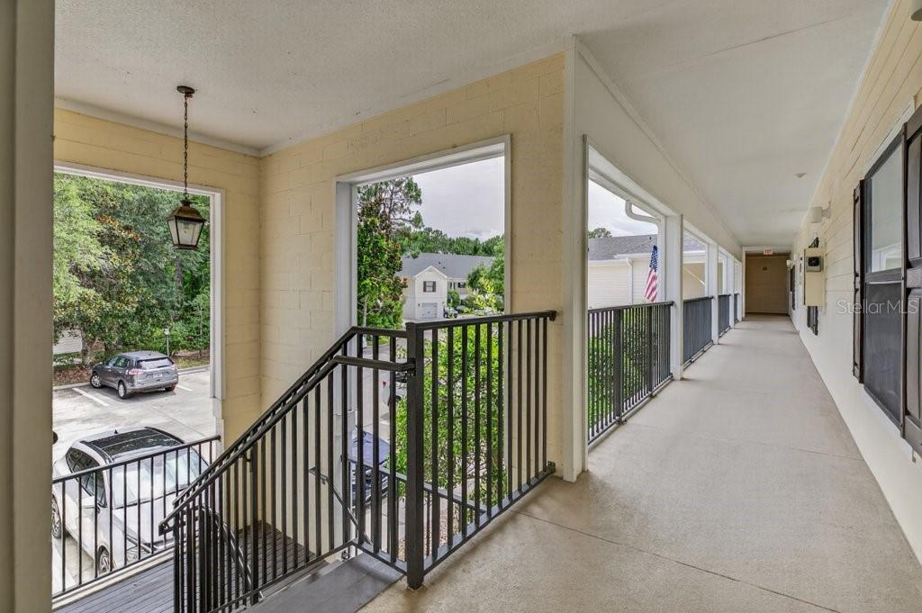 An outdoor covered walkway with a metal railing overlooks a parking lot and trees — 112 LAUREL WOOD WAY UNIT 205, ST AUGUSTINE, FL
