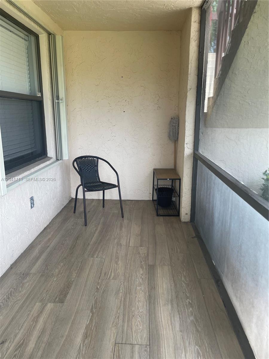 A screened-in balcony features wood-look flooring, a single black chair, and a small metal shelf — 7250 Golf Colony Ct # 102, Lake Worth FL 33467, LAKE WORTH, FL