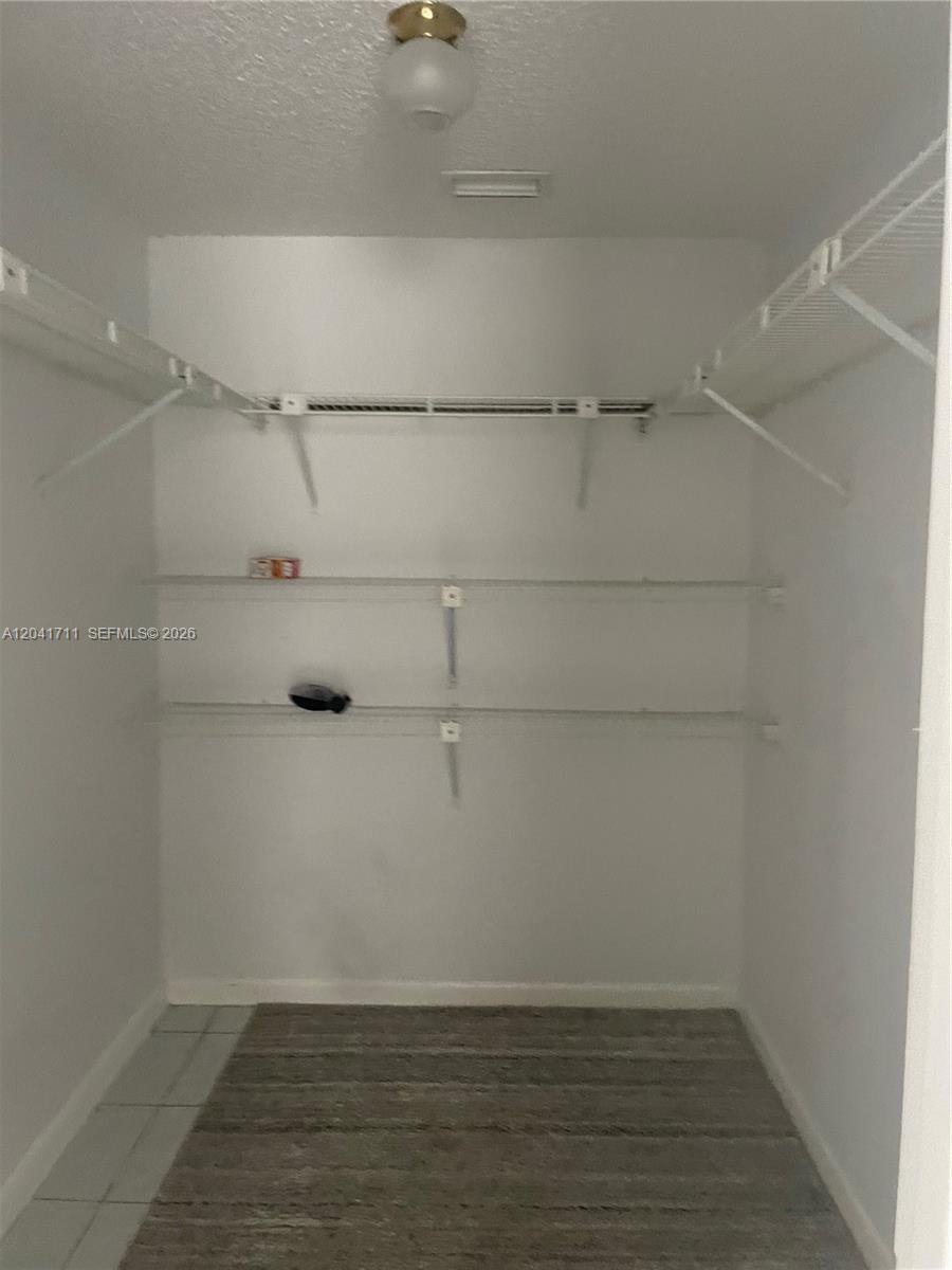 A walk-in closet features white wire shelving, a light fixture, and tiled flooring — 7250 Golf Colony Ct # 102, Lake Worth FL 33467, LAKE WORTH, FL
