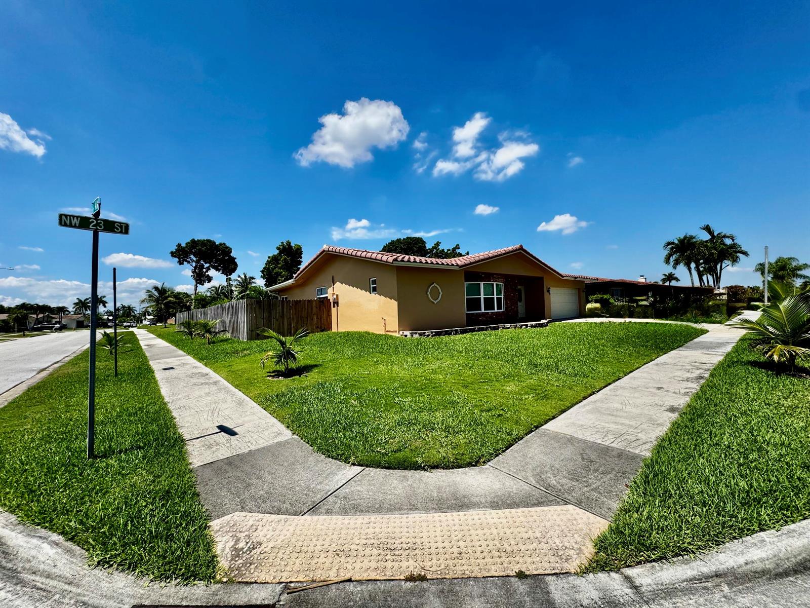 A tan, single-story house with a tiled roof sits on a corner lot with sidewalks — 6600 NW 23rd Street, Margate FL 33063, MARGATE, FL