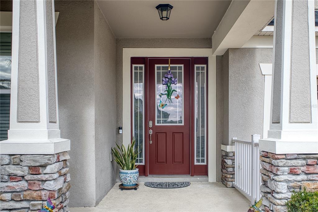 A red front door with a decorative glass insert sits on a covered stone porch — 3014 SERA BELLA WAY, KISSIMMEE, FL