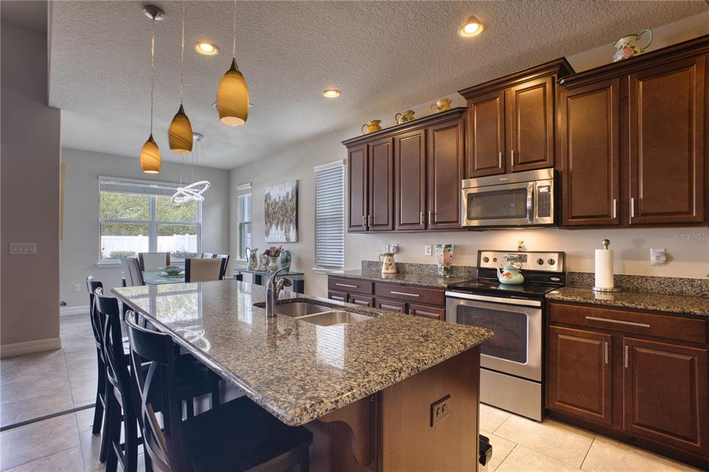 A kitchen features dark wood cabinets, granite countertops, a center island, and stainless steel appliances — 3014 SERA BELLA WAY, KISSIMMEE, FL