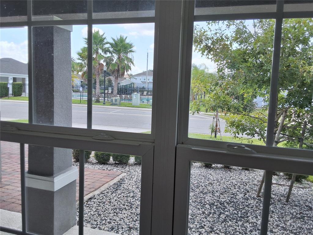 A view through a window shows a street, palm trees, and a community pool area — 4375 SILVER CREEK STREET, KISSIMMEE, FL