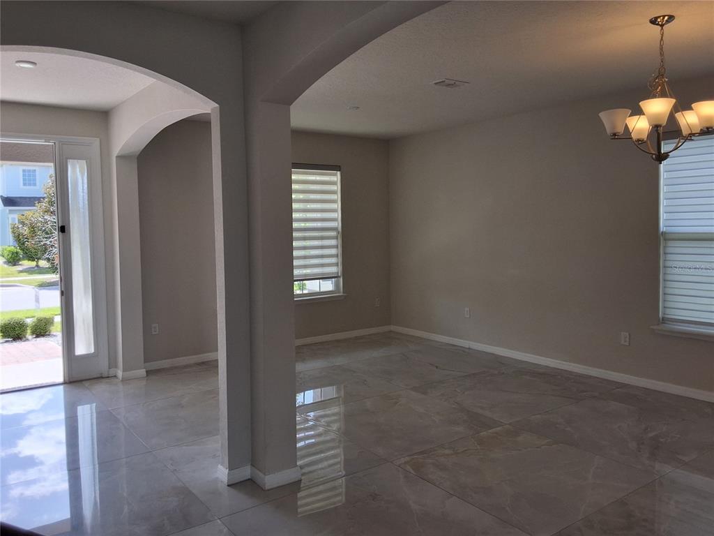An open-concept room features large light-colored floor tiles, beige walls, and a hanging chandelier — 4375 SILVER CREEK STREET, KISSIMMEE, FL