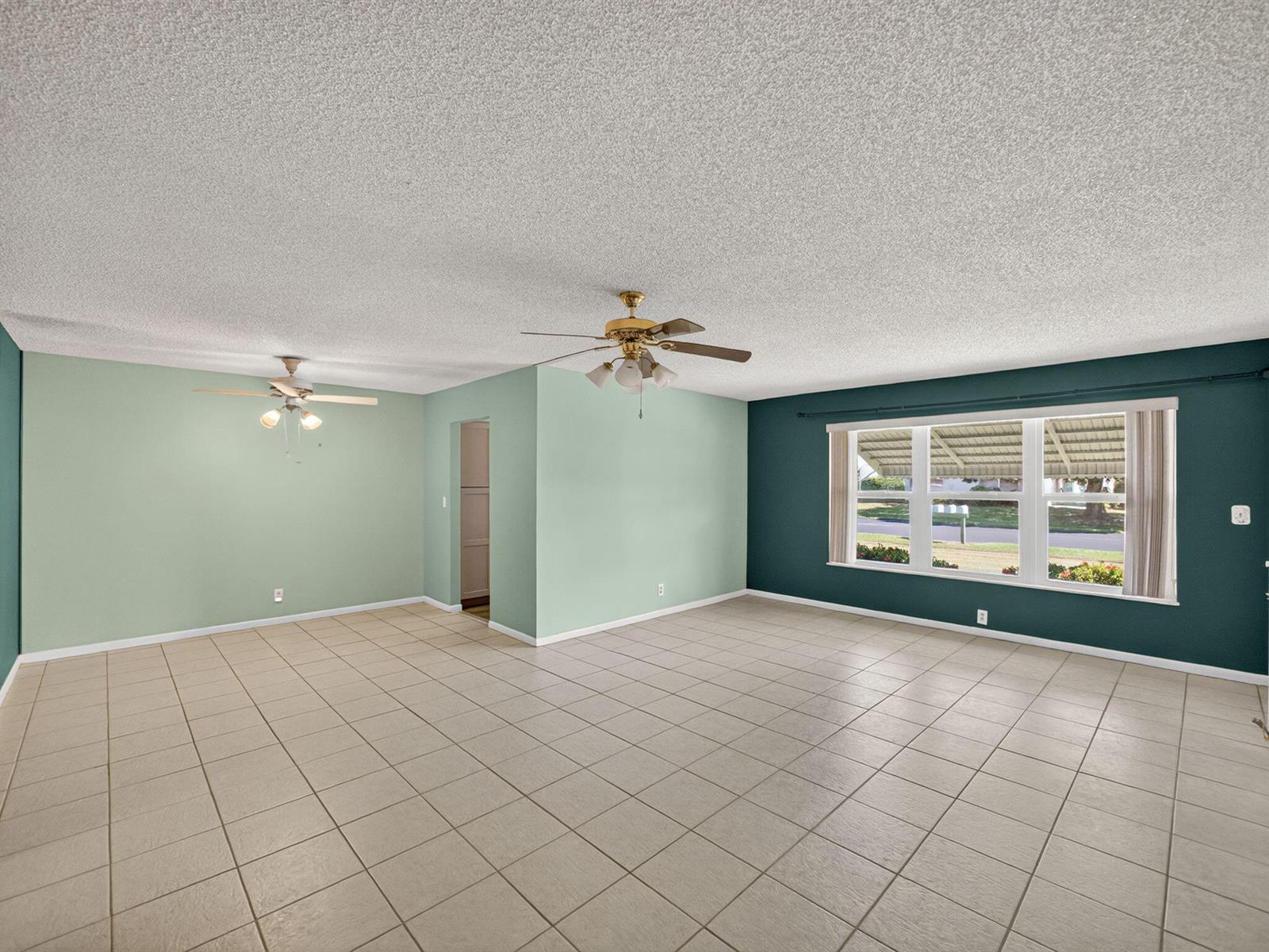 An empty living room features light green and dark teal walls, tile flooring, and ceiling fans — 111 Lakes End Drive # B, Fort Pierce FL 34982, FORT PIERCE, FL
