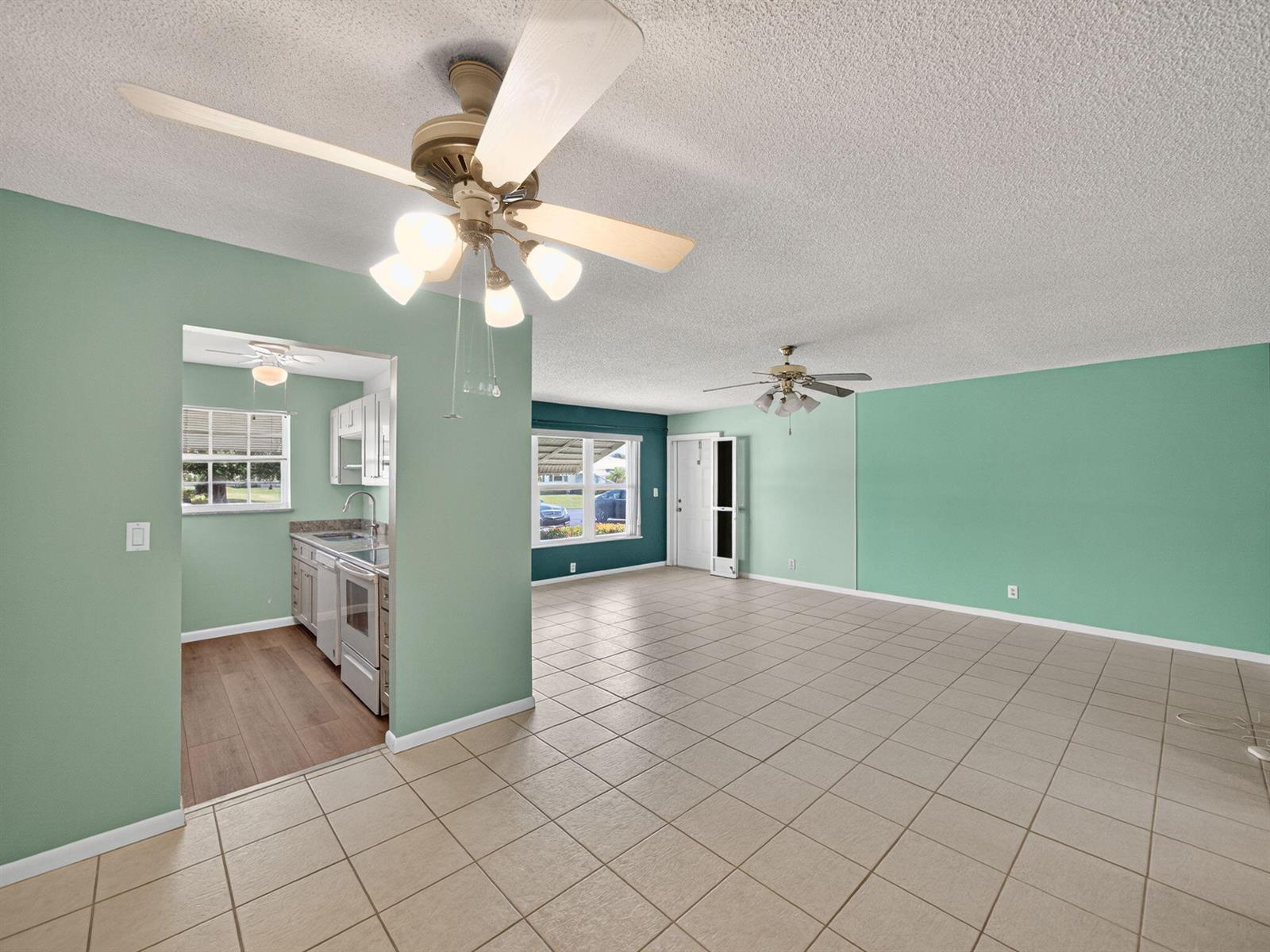 An open-concept living area with light green walls, tile flooring, and two ceiling fans — 111 Lakes End Drive # B, Fort Pierce FL 34982, FORT PIERCE, FL