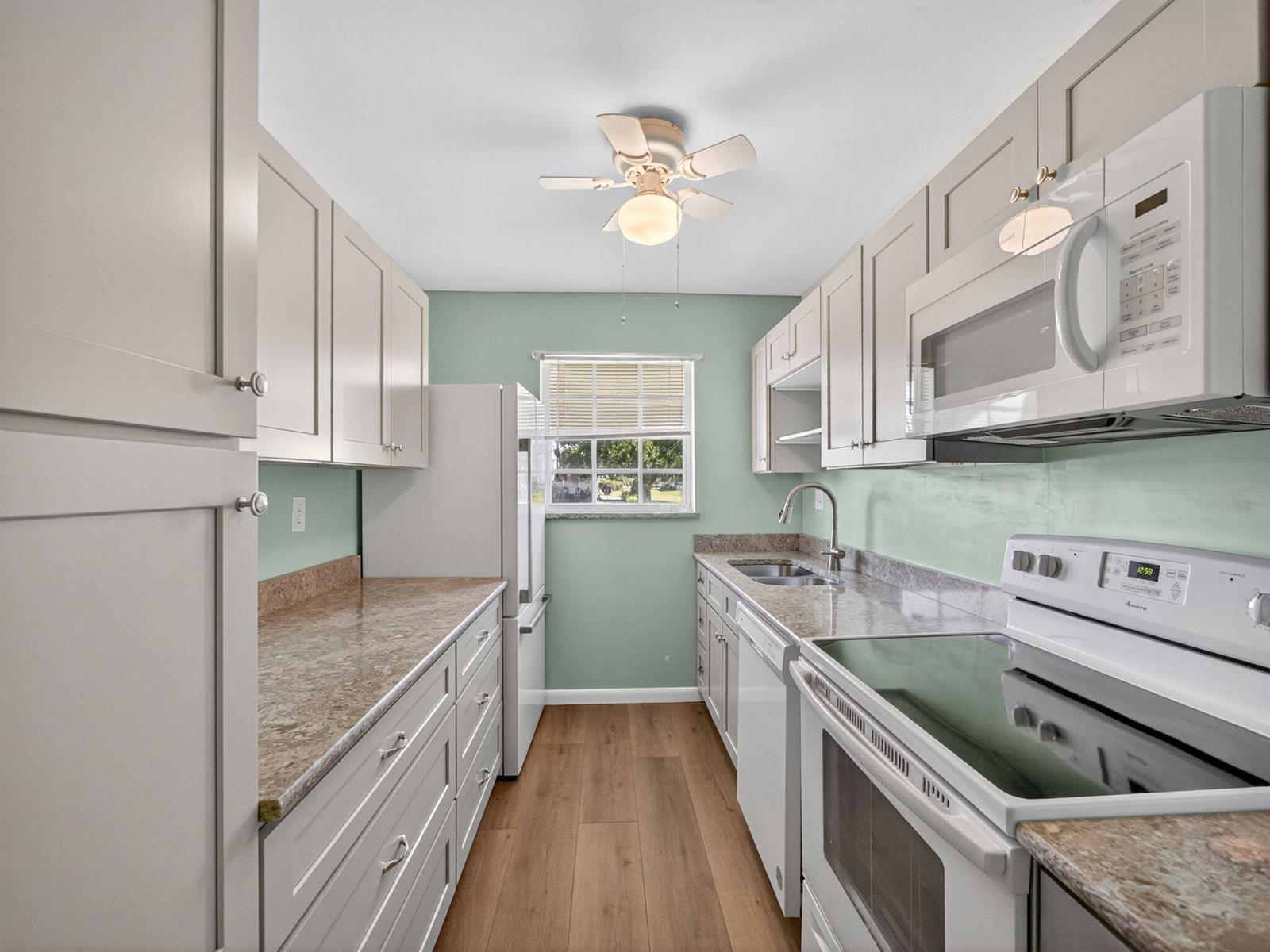 A galley kitchen features light-colored cabinetry, laminate countertops, stainless steel appliances, and mint green walls — 111 Lakes End Drive # B, Fort Pierce FL 34982, FORT PIERCE, FL
