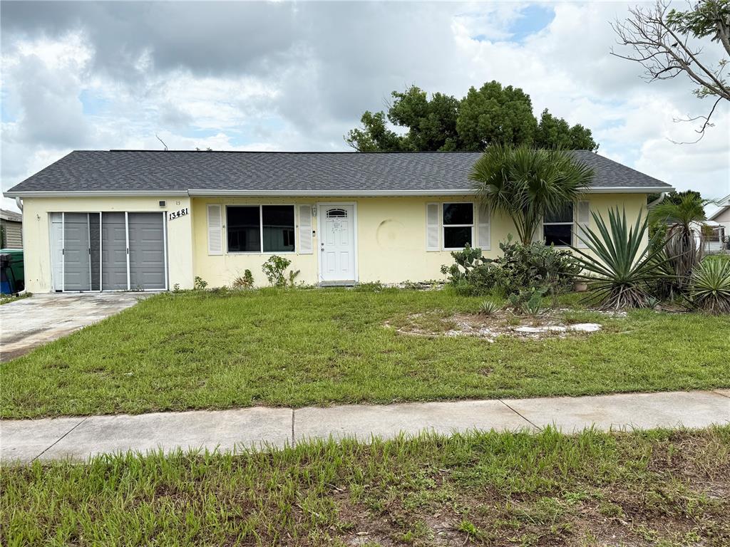 A single-story yellow house with a gray roof, a front door, and a garage door — 13481 DARNELL AVENUE, PORT CHARLOTTE, FL