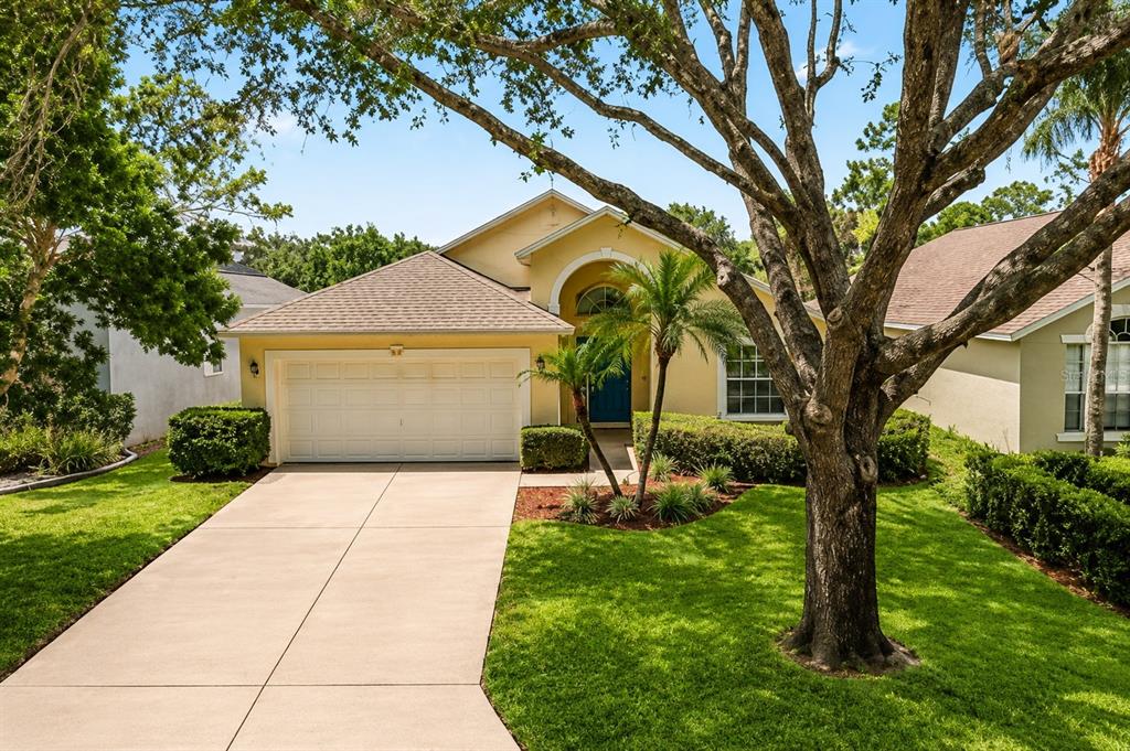 A yellow single-story house with a two-car garage and a large tree in the yard — 2263 MALLORY CIRCLE, HAINES CITY, FL