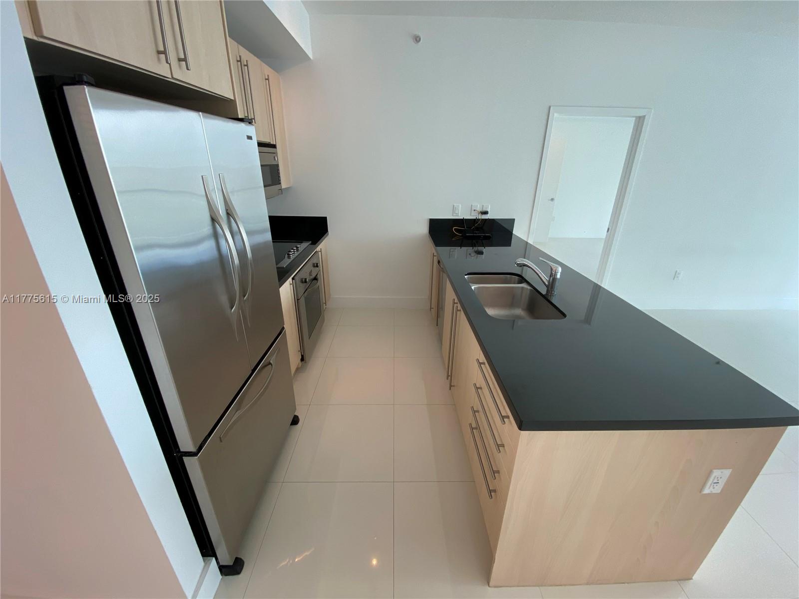 A modern kitchen features light wood cabinets, black countertops, stainless steel appliances, and tile flooring — 79 SW 12 ST, Miami FL 33130, MIAMI, FL