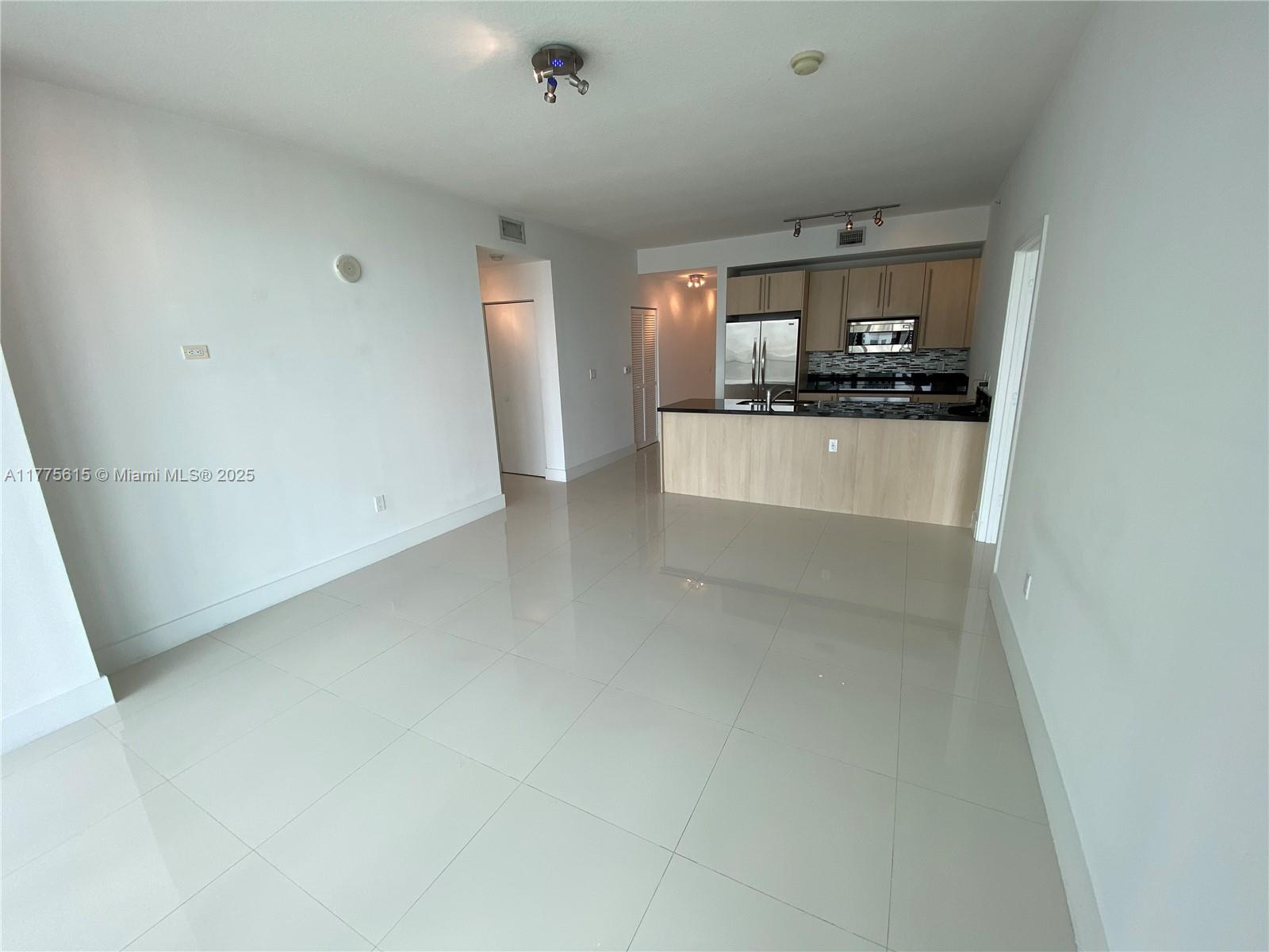 This open-concept living area features light-colored tile flooring and an adjacent kitchen with wood cabinetry — 79 SW 12 ST, Miami FL 33130, MIAMI, FL