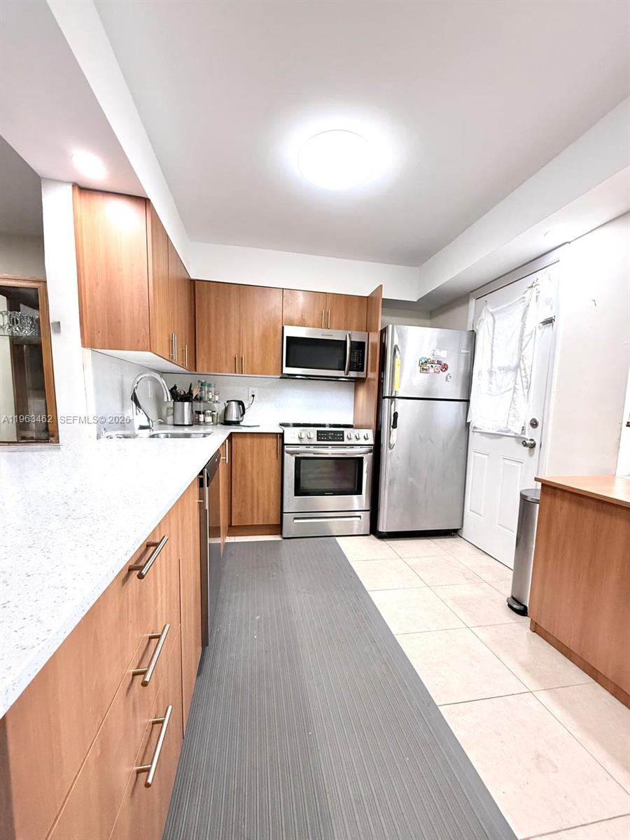 A kitchen features wood cabinets, stainless steel appliances, and white countertops with tile flooring — 1501 NE 191st St # C114, Miami FL 33179, MIAMI, FL