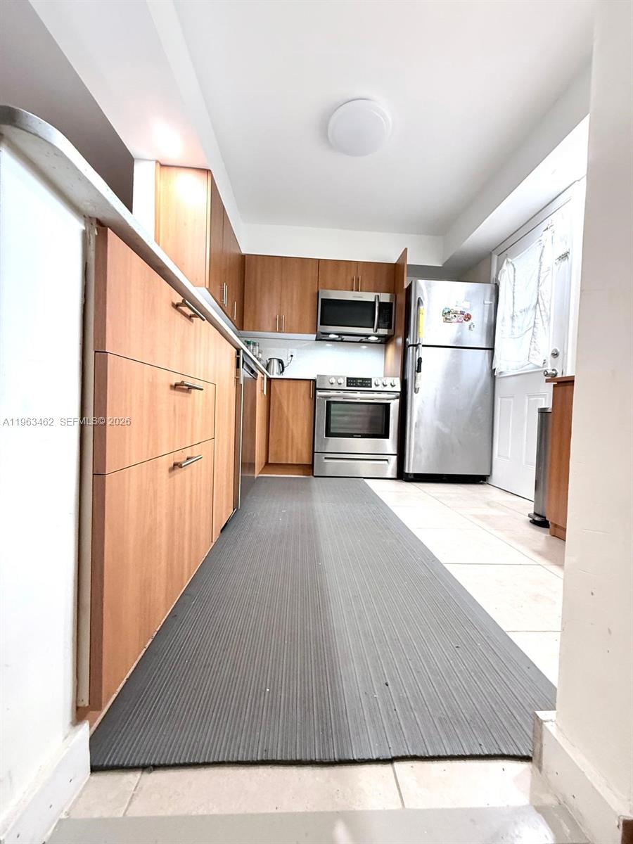 A galley kitchen features light wood cabinets, stainless steel appliances, and a gray floor mat — 1501 NE 191st St # C114, Miami FL 33179, MIAMI, FL