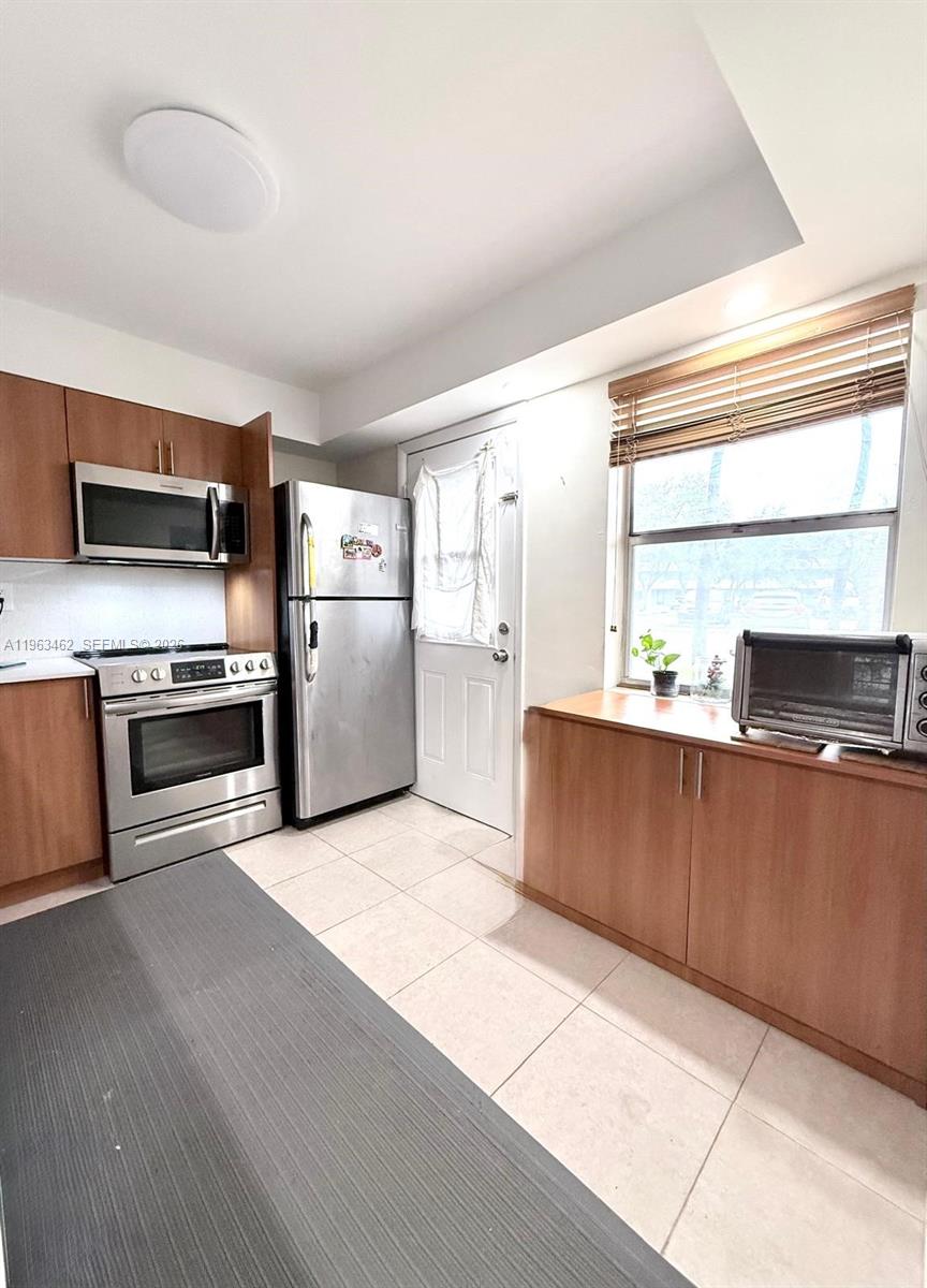 A kitchen features light wood cabinets, stainless steel appliances, tile flooring, and a window — 1501 NE 191st St # C114, Miami FL 33179, MIAMI, FL