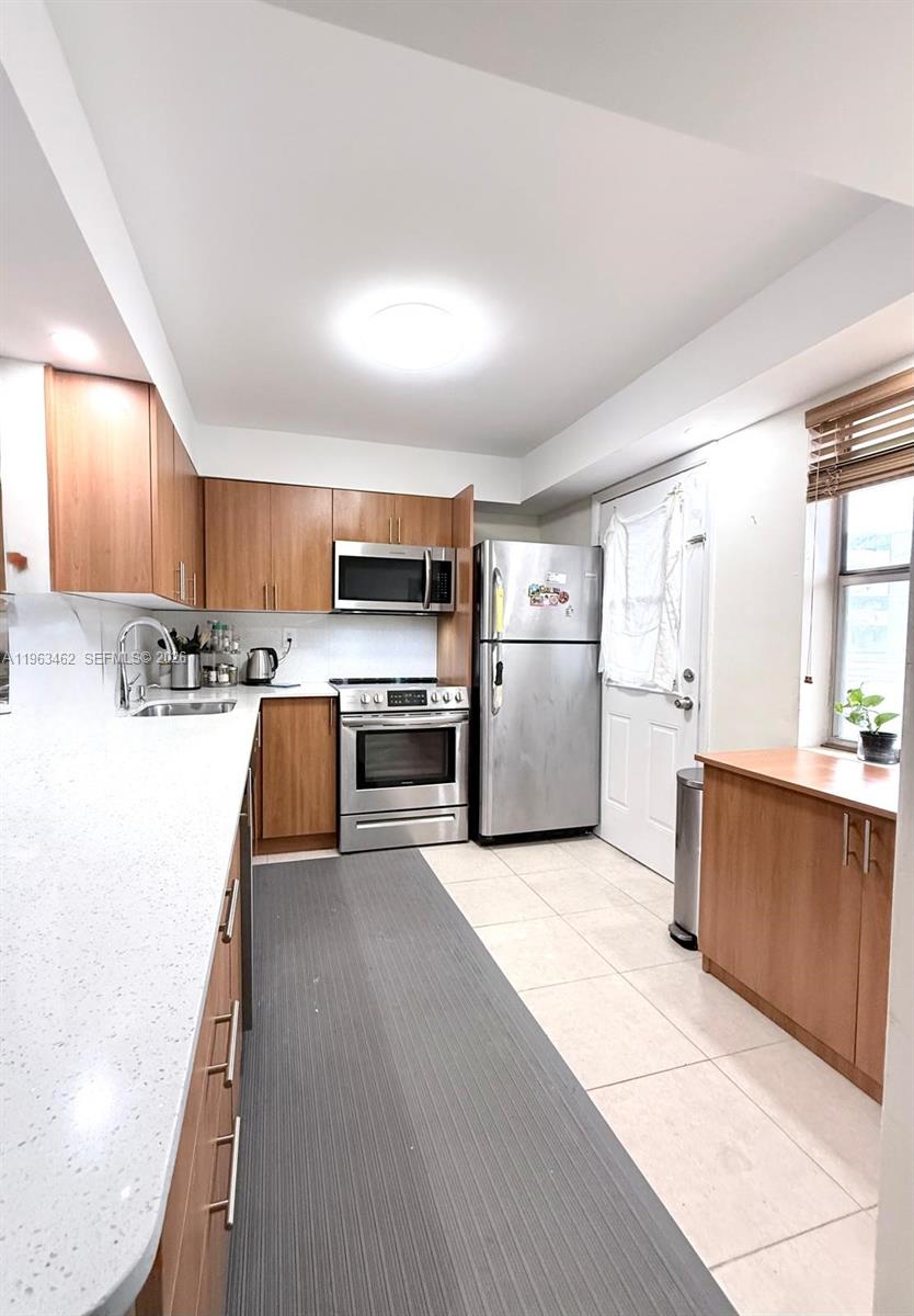 A kitchen features wood cabinets, stainless steel appliances, white countertops, and light-colored tile flooring — 1501 NE 191st St # C114, Miami FL 33179, MIAMI, FL