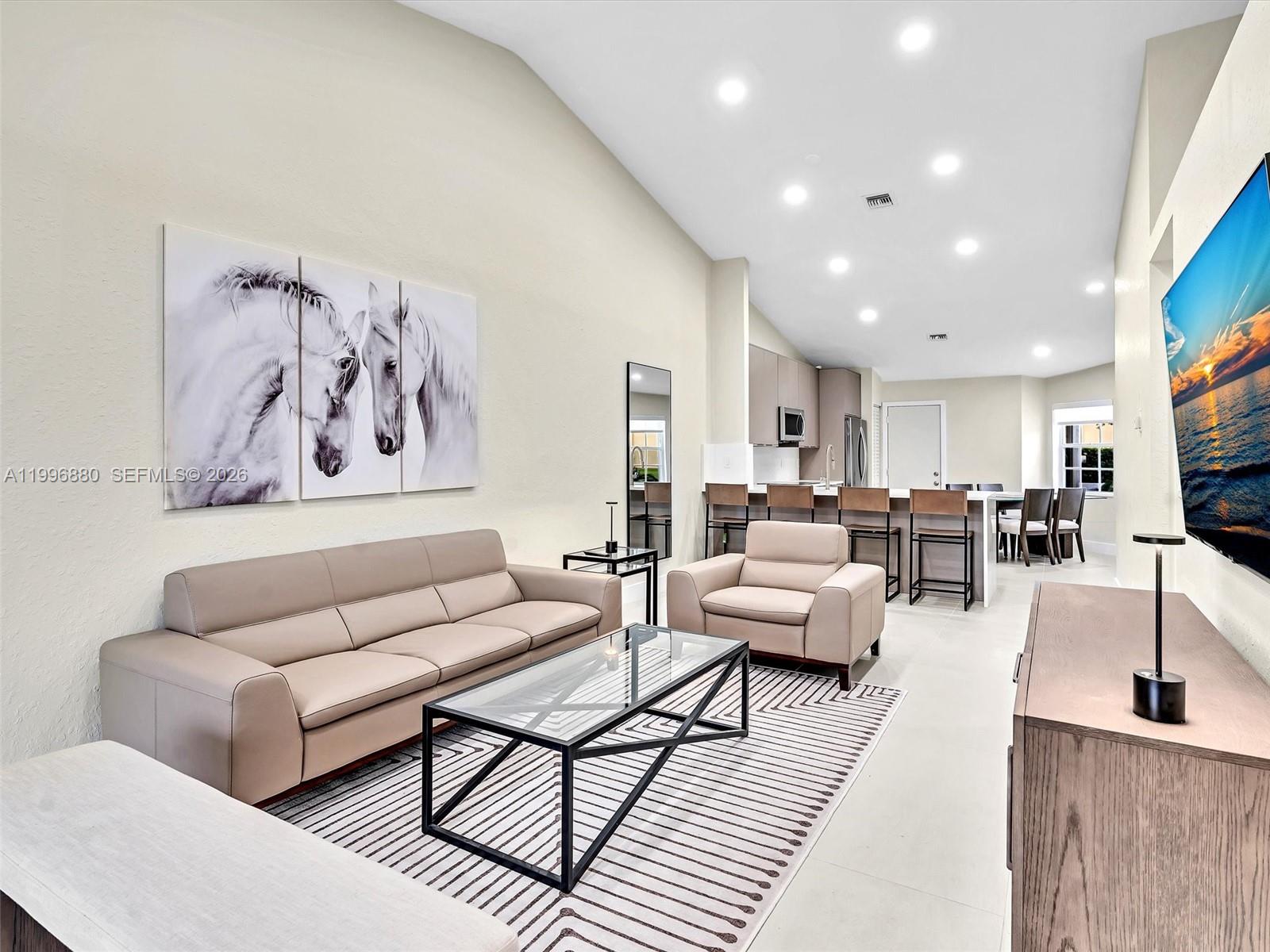 A living room with a beige sofa, armchair, glass coffee table, and an open kitchen — 15212 W Tranquility Lake Dr # 15212, Delray Beach FL 33446, DELRAY BEACH, FL