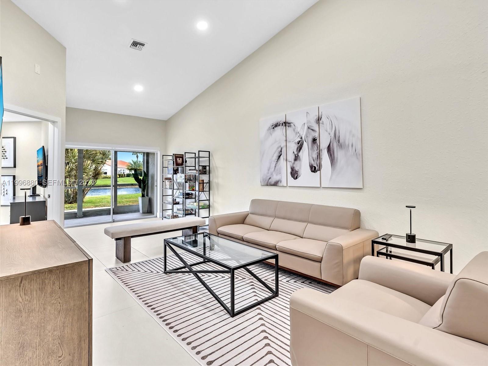 A living room features a beige sofa, glass coffee table, and horse wall art — 15212 W Tranquility Lake Dr # 15212, Delray Beach FL 33446, DELRAY BEACH, FL