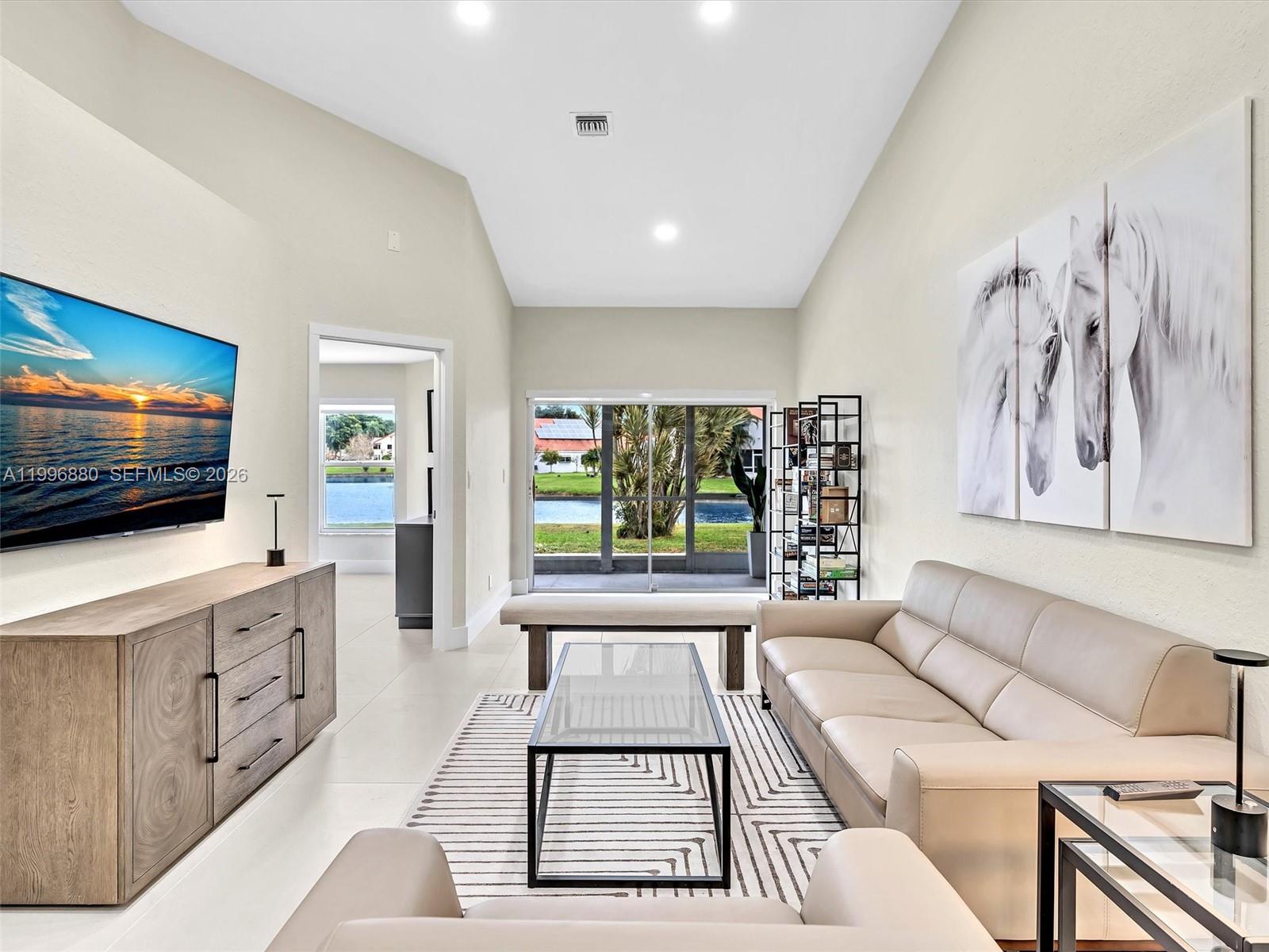 A living room features a vaulted ceiling, a wall-mounted television, and a view of water — 15212 W Tranquility Lake Dr # 15212, Delray Beach FL 33446, DELRAY BEACH, FL