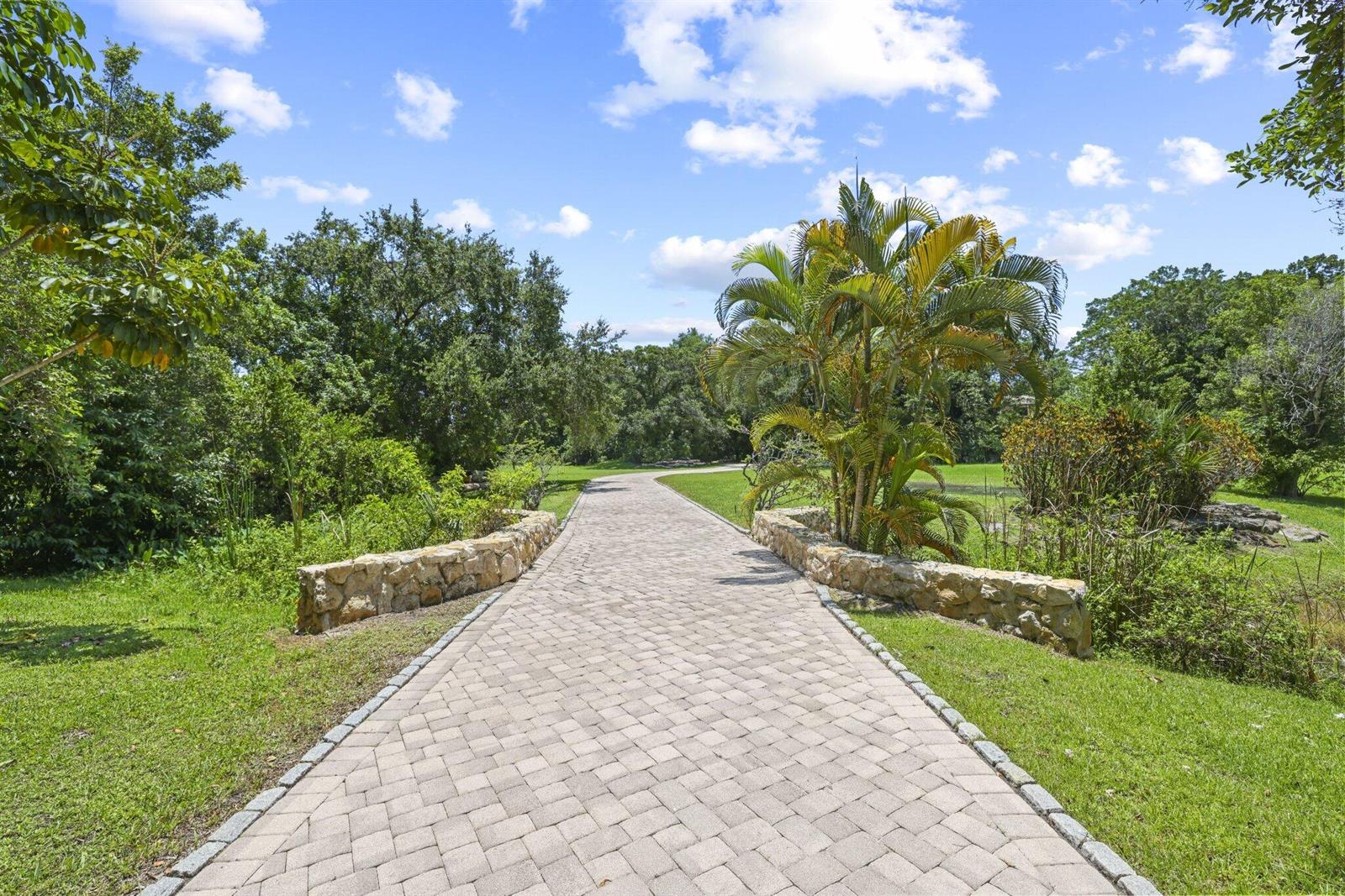 A paved stone walkway leads through a lush green landscape with palm trees and shrubs — 6001 Le Lac Road, Boca Raton FL 33496, BOCA RATON, FL