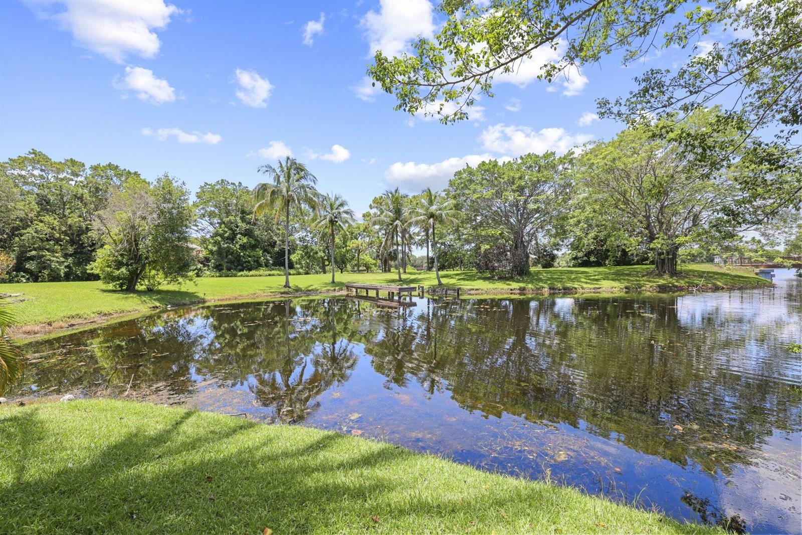 A small wooden dock sits on a pond surrounded by green grass and mature trees — 6001 Le Lac Road, Boca Raton FL 33496, BOCA RATON, FL