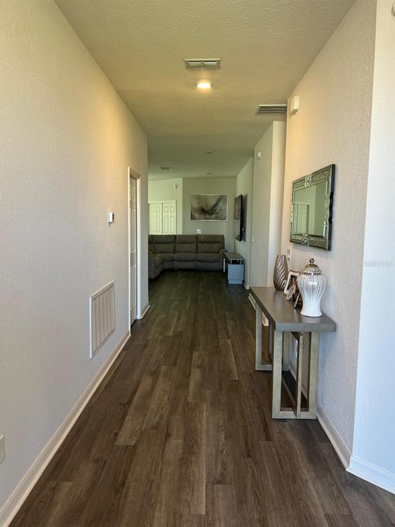 A hallway with wood-look flooring leads to a living room with a gray sectional sofa — 5966 WILDFLOWER FIELD WAY, ST CLOUD, FL
