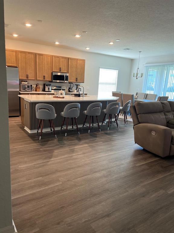 A kitchen features a large island with bar seating, light wood cabinets, and wood-look flooring — 5966 WILDFLOWER FIELD WAY, ST CLOUD, FL