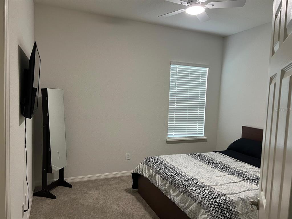 A bedroom features a bed with patterned bedding, a wall-mounted television, and a standing mirror — 5966 WILDFLOWER FIELD WAY, ST CLOUD, FL