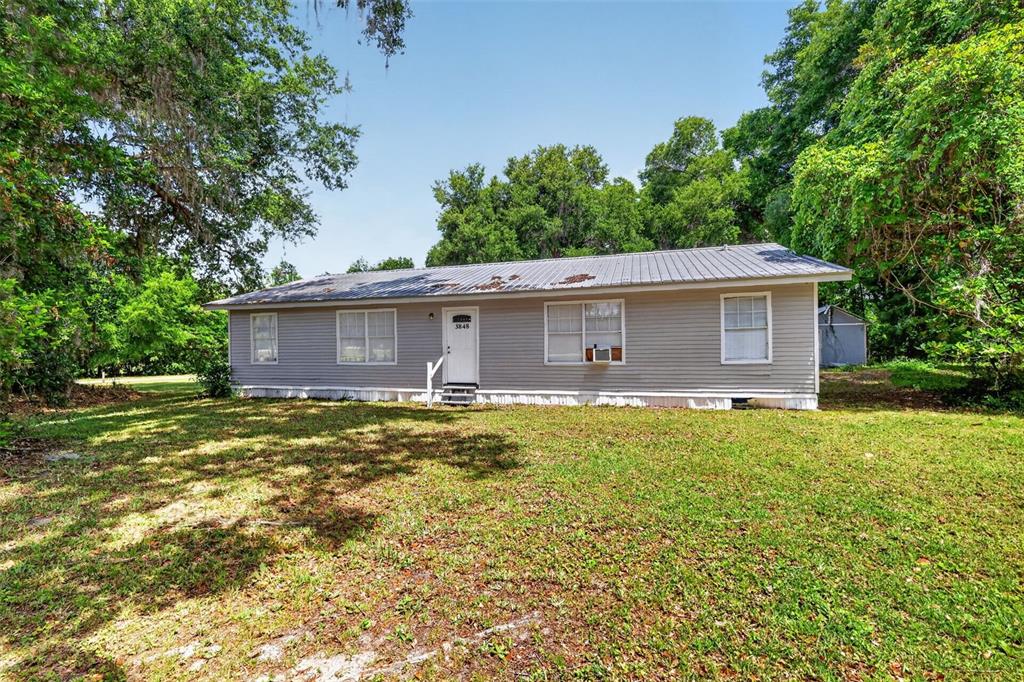 A single-story house with gray siding and a metal roof sits on a grassy lot — 3848 WARM SPRINGS AVENUE, WILDWOOD, FL