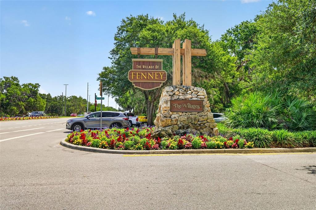 A stone monument sign for The Village of Fenney stands beside a road with landscaping — 3848 WARM SPRINGS AVENUE, WILDWOOD, FL