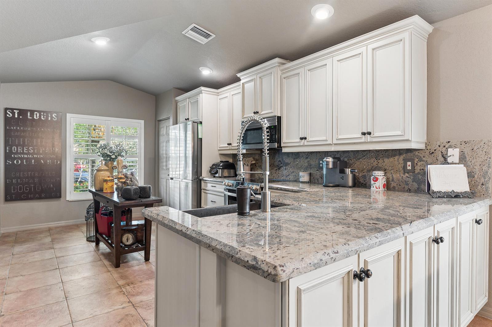 A kitchen features white cabinets, granite countertops, a stainless steel refrigerator, and tile flooring — 5318 Vernio Lane, Boynton Beach FL 33437, BOYNTON BEACH, FL