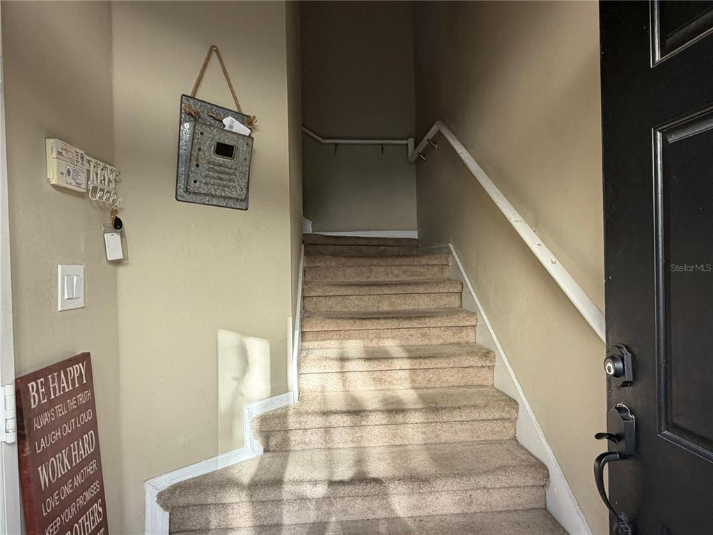 A carpeted staircase leads upward in a foyer with beige walls and a black door — 6488 S GOLDEN ROD UNIT 43A, ORLANDO, FL