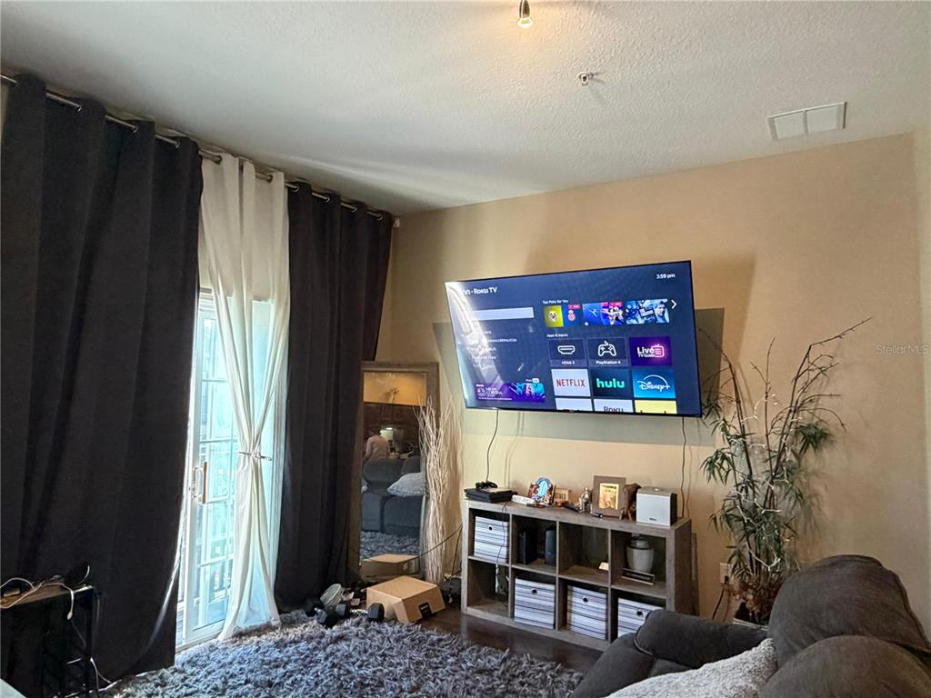 A living room features a wall-mounted television, a media console, and floor-to-ceiling curtains — 6488 S GOLDEN ROD UNIT 43A, ORLANDO, FL