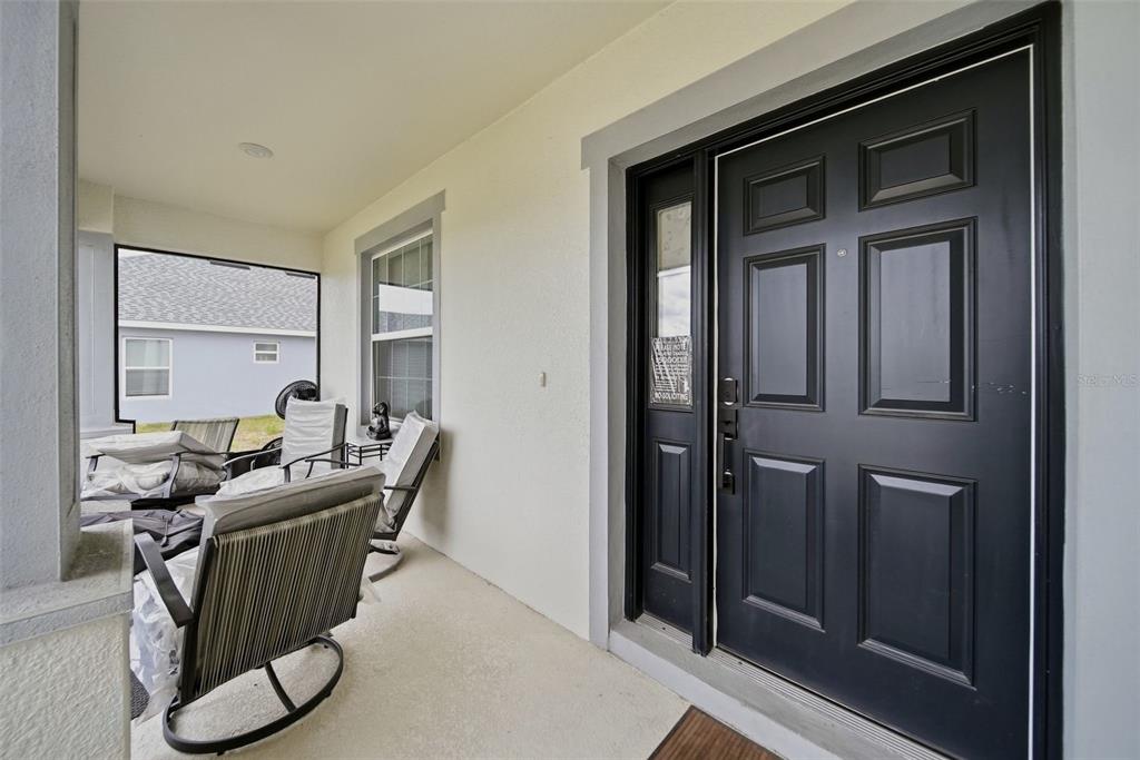 A covered front porch features a black front door with a side light and patio furniture — 1862 DAYSTAR DRIVE, HAINES CITY, FL