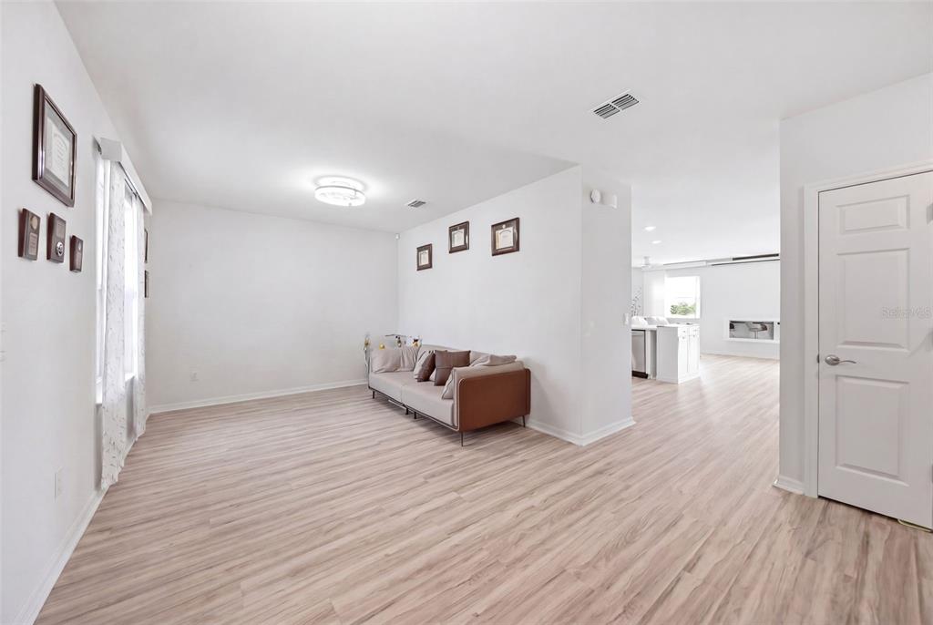 A living room with light wood-look flooring, white walls, and a sofa against a partition wall — 1862 DAYSTAR DRIVE, HAINES CITY, FL