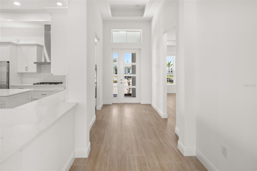 A bright entryway features light wood-look tile flooring, white walls, and a modern glass-paneled front door — 832 BLUE SHELL LOOP, SARASOTA, FL
