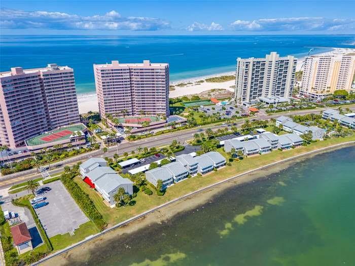 An aerial view shows high-rise apartment buildings, low-rise residential units, and a beach along water — 1351 GULF BOULEVARD UNIT 118, CLEARWATER BEACH, FL