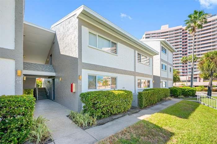 A two-story residential building with a covered walkway and manicured hedges under a blue sky — 1351 GULF BOULEVARD UNIT 118, CLEARWATER BEACH, FL