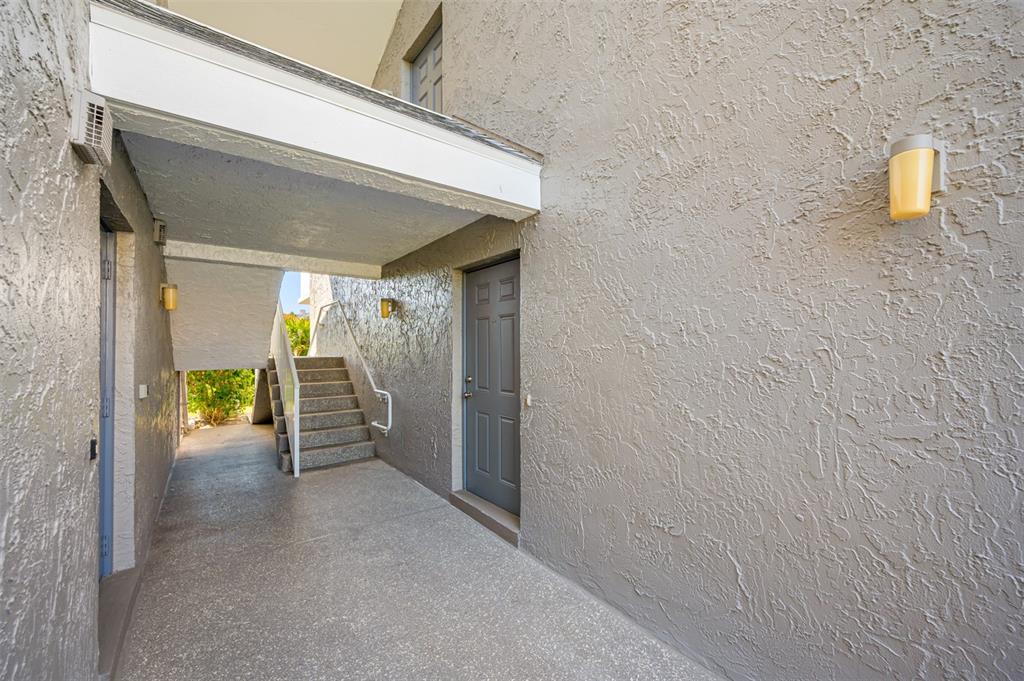 An exterior view of a building entrance with a gray door, concrete stairs, and stucco walls — 1351 GULF BOULEVARD UNIT 118, CLEARWATER BEACH, FL