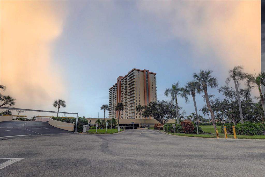 A tall, multi-story residential building stands behind a paved entrance with palm trees — 4900 BRITTANY DRIVE S UNIT 1409, ST PETERSBURG, FL