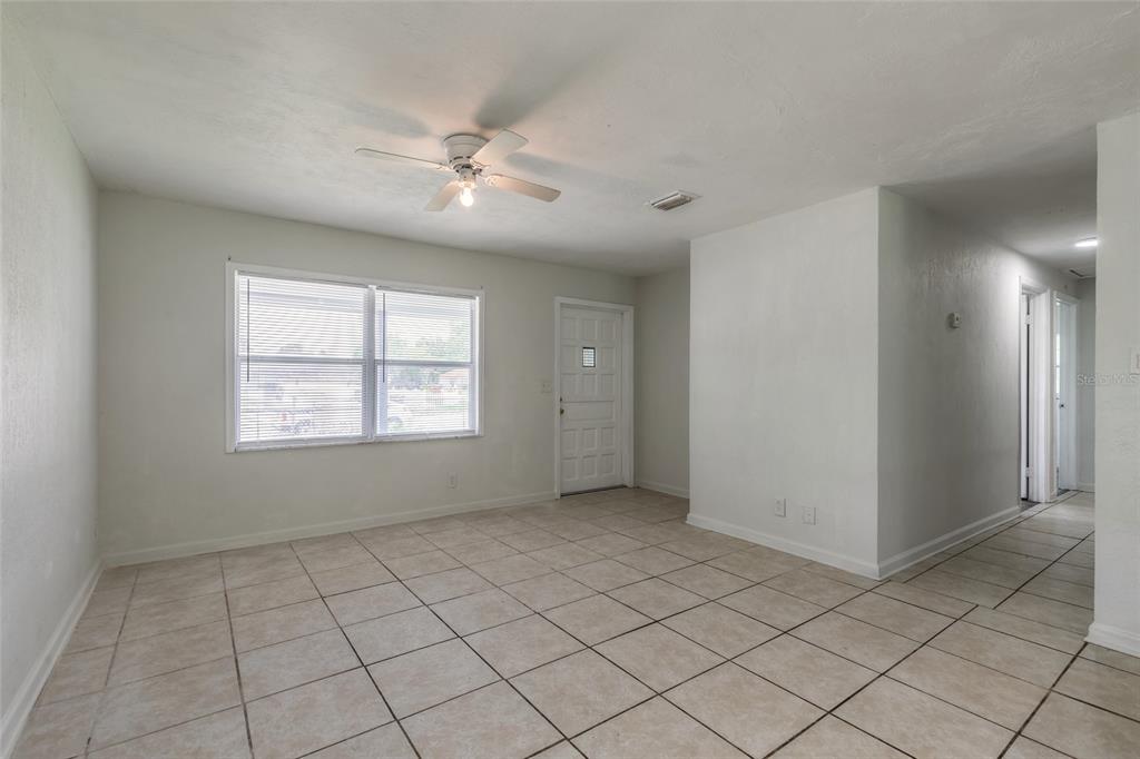 A living room with light-colored tile flooring, a ceiling fan, and a white front door — 901 LOCKHART STREET, DAYTONA BEACH, FL