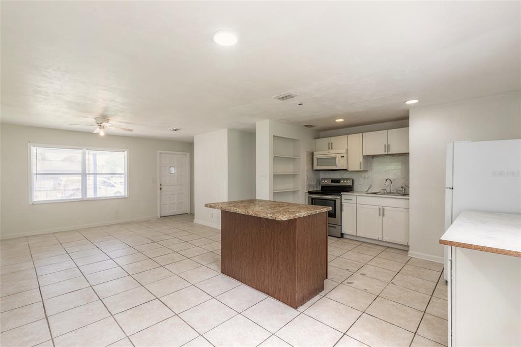 An open-concept kitchen and living area featuring white cabinets, tile flooring, and a kitchen island — 901 LOCKHART STREET, DAYTONA BEACH, FL