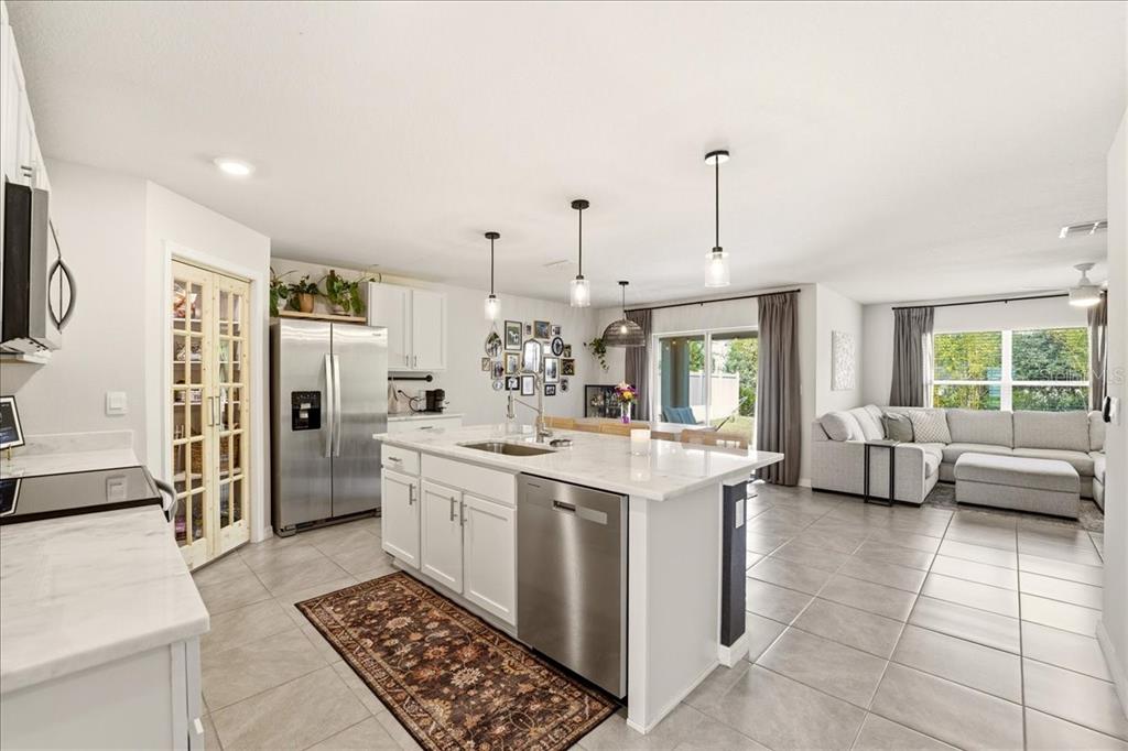 A modern kitchen features white cabinetry, a marble-topped island with bar seating, and tile flooring — 12273 MOUNTAIN ISLAND TRAIL, PARRISH, FL