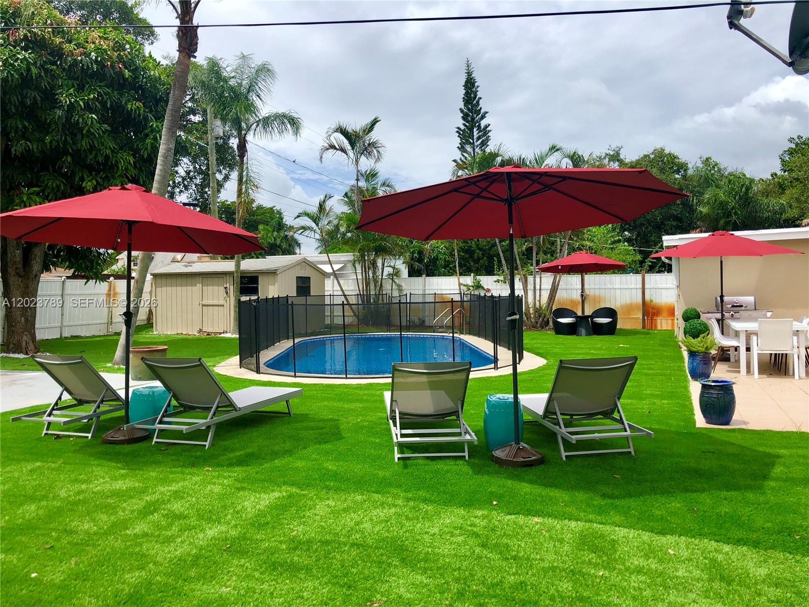 A backyard features a swimming pool, lounge chairs, red umbrellas, and artificial turf — 1918 Liberty St # 0, Hollywood FL 33020, HOLLYWOOD, FL