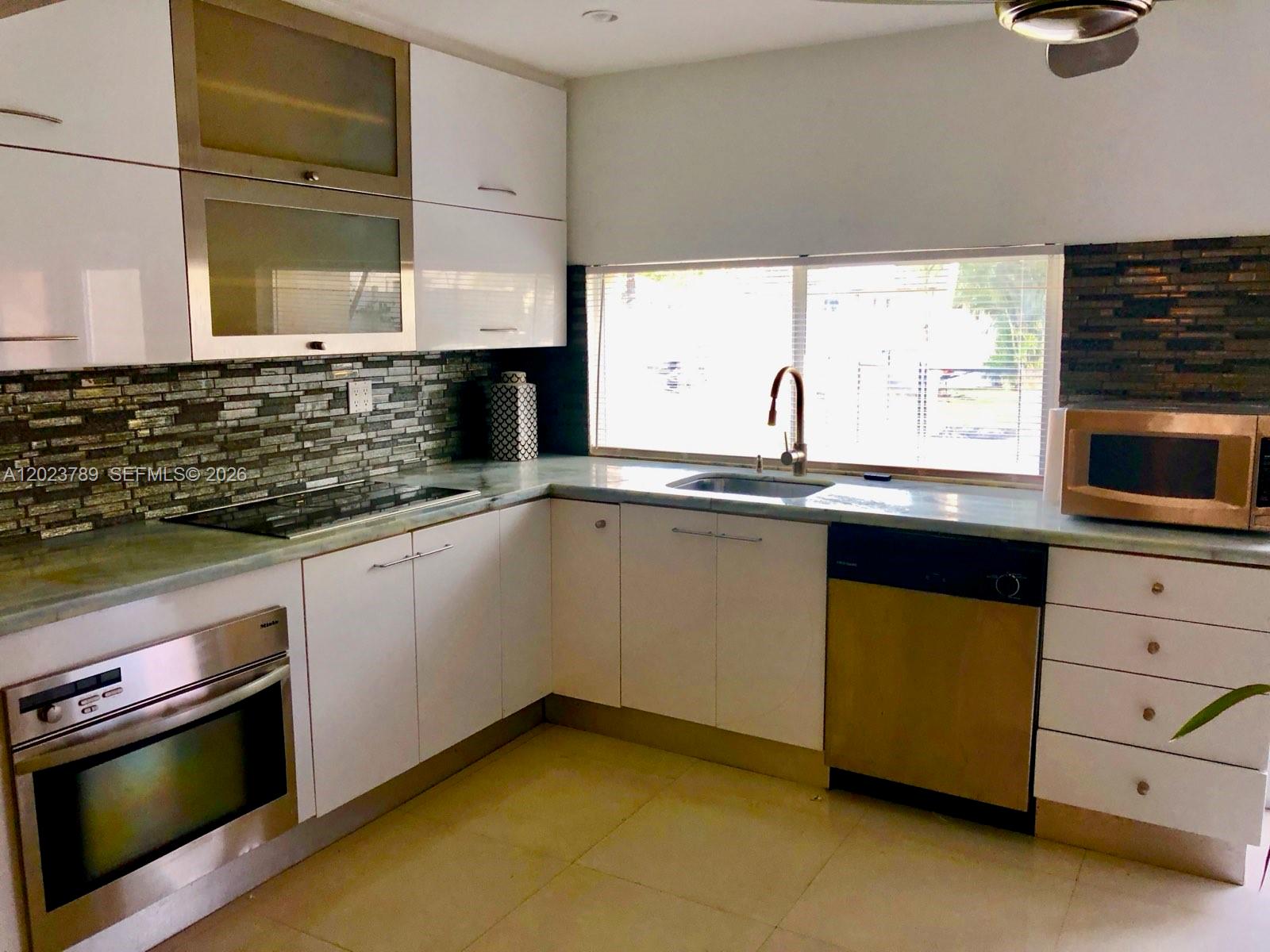 A kitchen features white cabinets, a stone backsplash, stainless steel appliances, and a window — 1918 Liberty St # 0, Hollywood FL 33020, HOLLYWOOD, FL