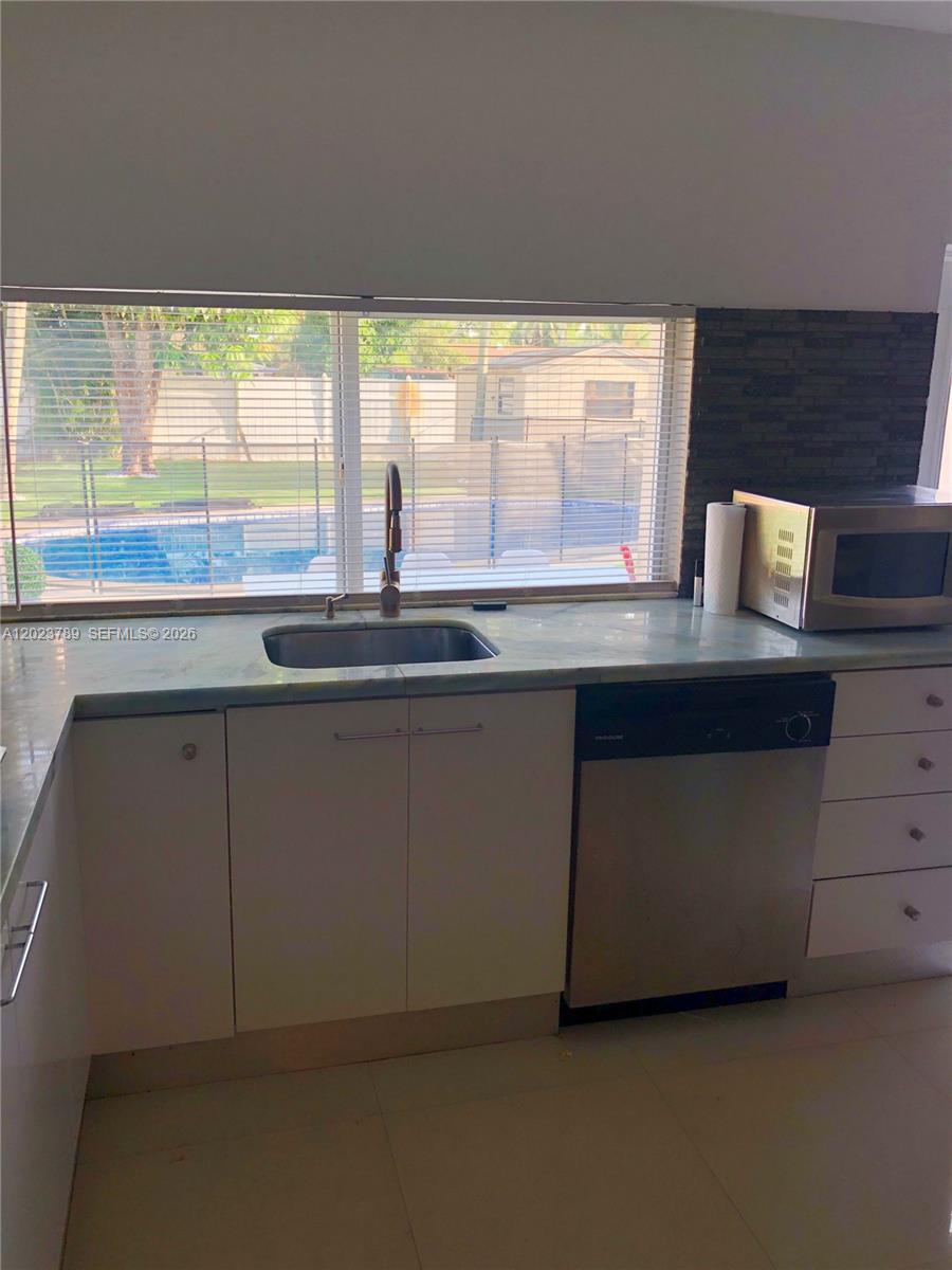 A kitchen features white cabinets, a stainless steel dishwasher, and a window overlooking a pool — 1918 Liberty St # 0, Hollywood FL 33020, HOLLYWOOD, FL