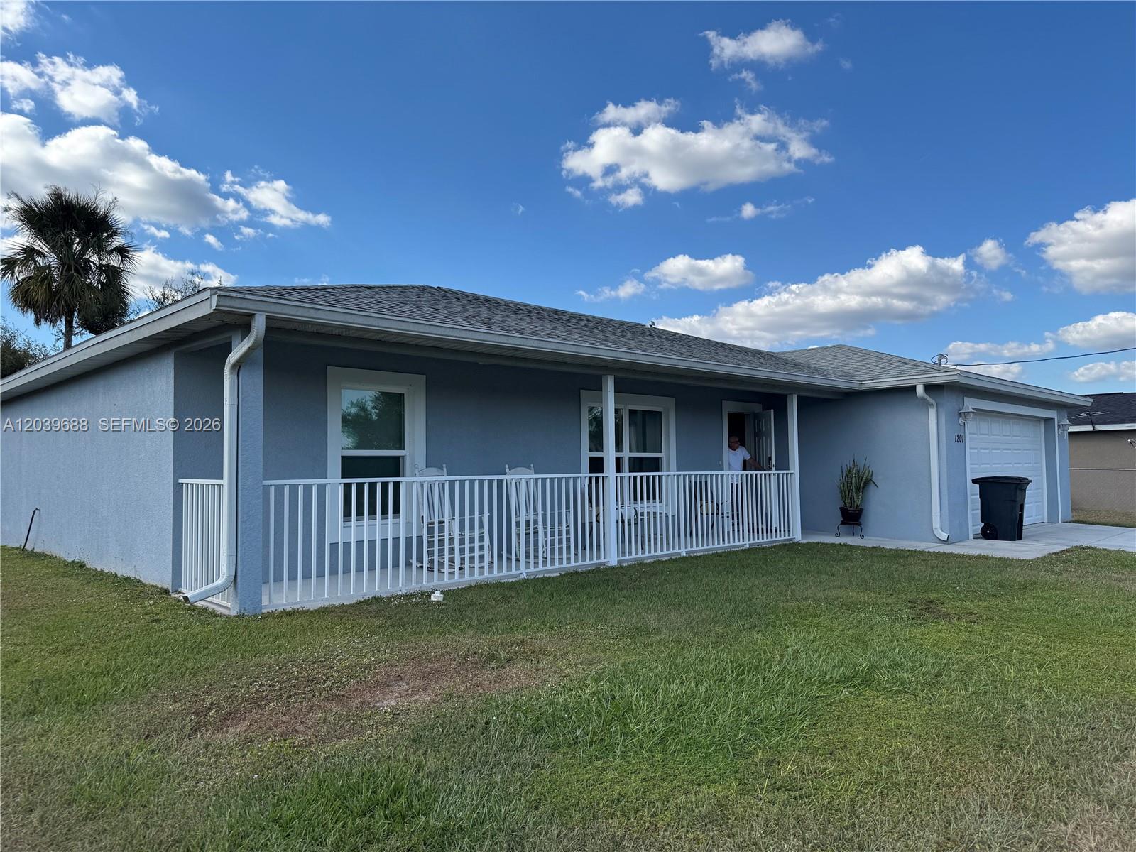 A single-story blue house features a white porch railing, a garage, and a front lawn — 1201 BANJO CT, La Belle FL 33935, LA BELLE, FL