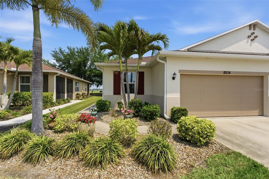 A single-story house exterior features a beige garage, palm trees, and a landscaped front yard — 8834 TUSCANY ISLES DRIVE, PUNTA GORDA, FL